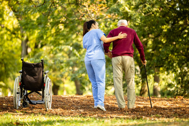 nursing assistant helping elderly man to walk with walking cane.