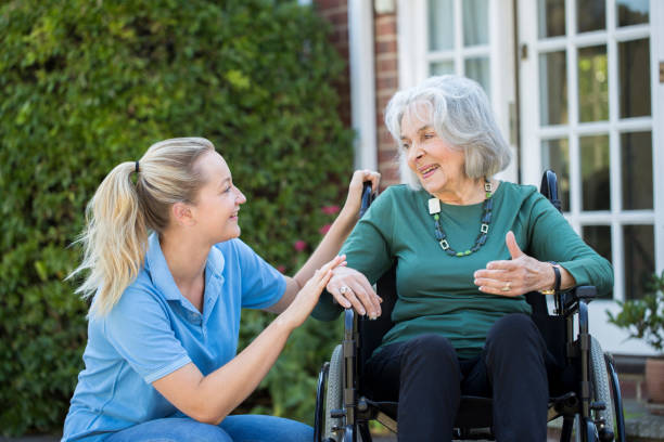 carer pushing senior woman in wheelchair outside home